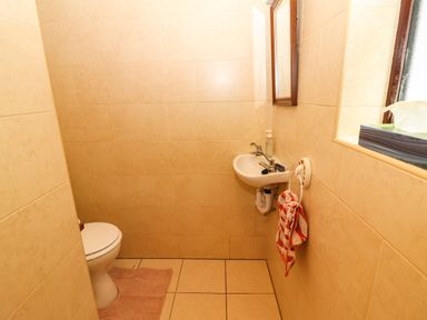 A small bathroom with a toilet a wall-mounted sink a mirror and a window with a tissue box at Brendans Cottage in Valentia Island County Kerry