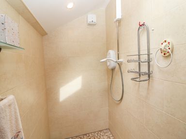 A tiled shower area with a wall-mounted electric shower unit and metal storage racks at Brendans Cottage in Valentia Island County Kerry