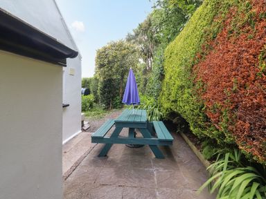 An outdoor area with a green picnic table and a closed purple umbrella next to a white building and trimmed hedges at Brendans Cottage in Valentia Island County Kerry