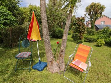 A garden with two chairs one with an orange striped fabric and a pillow and the other metal with a cushion next to a tree and a closed red and yellow umbrella at Brendans Cottage Valentia Island County Kerry