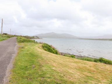 A roadside path beside a body of water with grassy banks and hills in the background at Brendans Cottage in Valentia Island County Kerry
