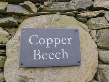 A sign reading Copper Beech mounted on a stone wall at Copper Beech Cottage in Torver