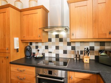 A kitchen with wooden cabinets and an electric stove at Copper Beech Cottage in Torver