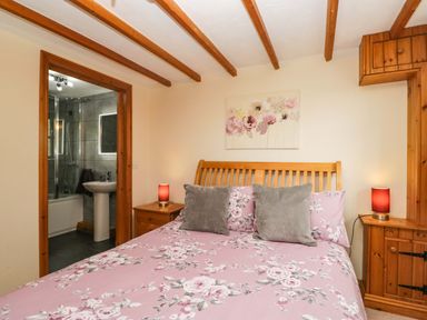 A bedroom with a bed and bathroom access at Copper Beech Cottage in Torver