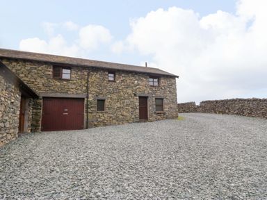 An outdoor view of a stone building with gravel area at Copper Beech Cottage in Torver
