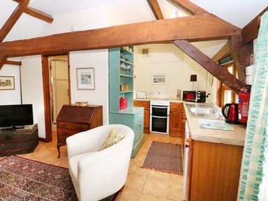 A small kitchen and sitting area with wooden beams a white armchair a television and kitchen appliances at The Pottery in Urchfont near Devizes