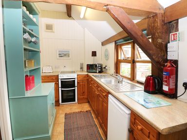 A kitchen with wooden cabinets a white stove a sink and various appliances including a red kettle and microwave at The Pottery in Urchfont near Devizes