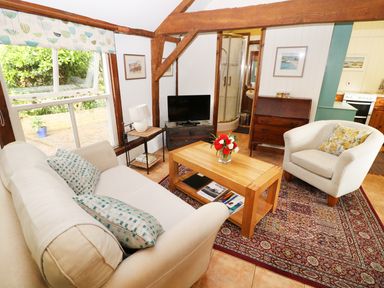 A sitting room with sofa armchair wooden table flowers television and visible kitchen area at The Pottery in Urchfont near Devizes