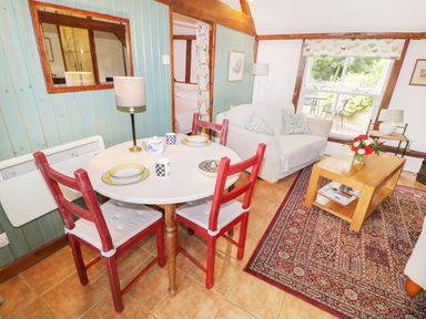 A dining area with a round table and red chairs next to a living room with a white sofa and wooden coffee table at The Pottery in Urchfont near Devizes