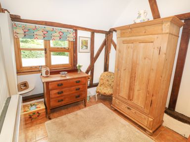 A room with a wooden wardrobe a chest of drawers a patterned chair and a floral window blind at The Pottery in Urchfont near Devizes
