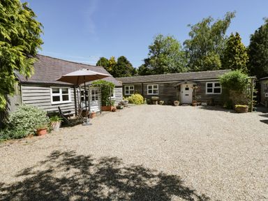A courtyard with gravel ground surrounded by wooden buildings and various potted plants at The Pottery in Urchfont near Devizes
