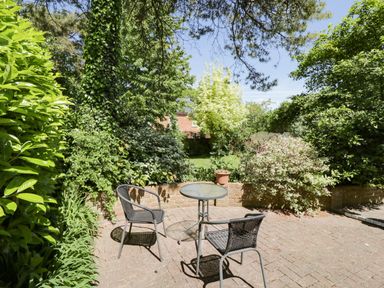 A patio with a round glass table and two metal chairs surrounded by greenery at The Pottery in Urchfont near Devizes