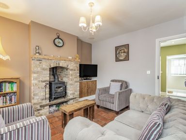 A living room with a brick fireplace and wood stove two striped armchairs a beige sofa a wooden coffee table a TV and a bookshelf at Fisher Cottage in Hornsea