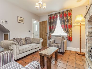 A living room with a beige sofa striped armchairs wooden coffee table floral curtains and a floor lamp at Fisher Cottage in Hornsea