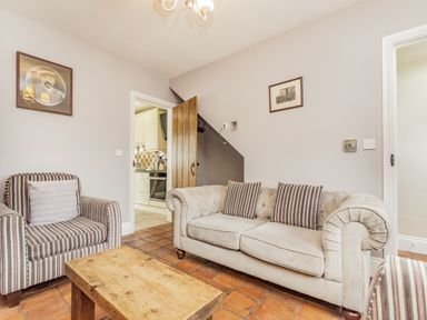 A living room with a striped armchair a wooden table and a beige sofa with striped cushions at Fisher Cottage in Hornsea