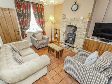 A living room with a sofa and armchairs around a wooden coffee table and a brick fireplace at Fisher Cottage in Hornsea