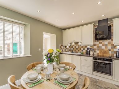 A kitchen with a round wooden table set for four and beige cabinets at Fisher Cottage in Hornsea