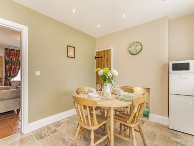 A dining area with a round wooden table set for four next to a white fridge with microwave at Fisher Cottage in Hornsea