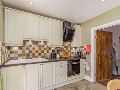 A kitchen with cream cabinets a tiled backsplash a sink an oven and a wooden door at Fisher Cottage in Hornsea