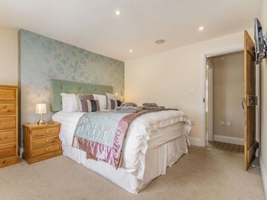 A bedroom with a bed with pillows and folded towels bedside tables a lamp a chest of drawers a door and a wall-mounted television at Fisher Cottage in Hornsea