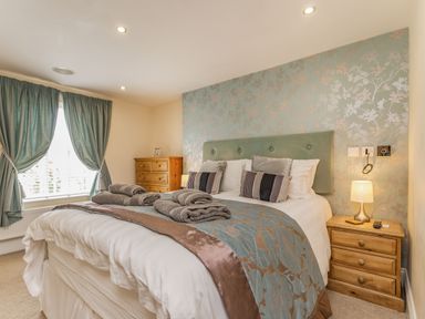 A bedroom with a double bed with folded towels bedside tables and a wooden chest of drawers at Fisher Cottage in Hornsea