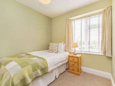 A small bedroom with a single bed a bedside table with a lamp and a window with curtains at Fisher Cottage in Hornsea