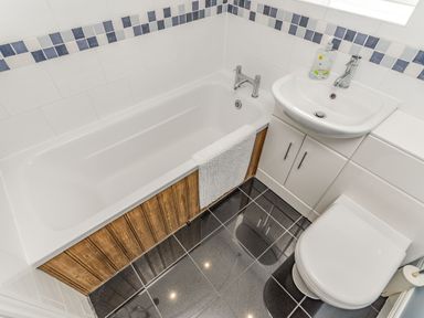 A bathroom with a bathtub with a wooden panel a sink with a cabinet and a toilet at Fisher Cottage in Hornsea