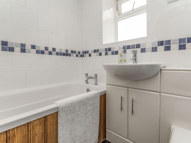 A bathroom with a bathtub with a white towel a sink with soap dispenser and storage cabinets at Fisher Cottage in Hornsea