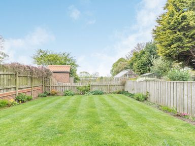 A garden with a lawn greenhouse and wooden fences at Fisher Cottage in Hornsea