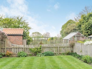 A backyard with green lawn wooden fence brick shed and glass greenhouse at Fisher Cottage in Hornsea