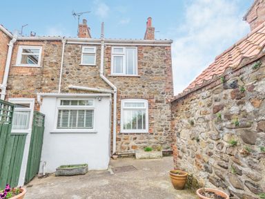 Exterior view of a stone cottage with multiple windows and flower pots in a paved courtyard at Fisher Cottage in Hornsea