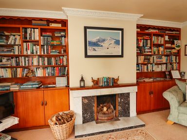 A room with bookshelves fireplace basket of firewood and a sofa at The Lodge Churchtown near Beaufort County Kerry