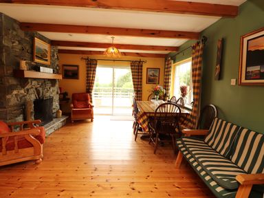 A dining room with wooden floor stone fireplace striped sofa checkered curtains and table at The Lodge Churchtown near Beaufort County Kerry