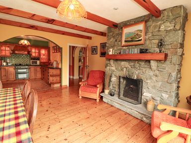 A living room with wooden furniture and a stone fireplace connected to a kitchen at The Lodge in Churchtown near Beaufort County Kerry