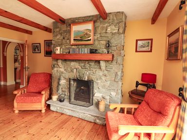 A sitting room with stone fireplace two wooden armchairs and framed pictures at The Lodge in Churchtown near Beaufort County Kerry