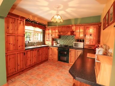 A kitchen with wooden cabinets green tiled backsplash black countertops and tiled floor at The Lodge in Churchtown near Beaufort County Kerry