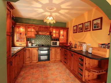 A kitchen with wooden cabinets tiled floor and framed pictures on the wall at The Lodge in Churchtown near Beaufort County Kerry
