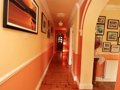 A hallway with wooden floor and framed pictures on the walls leading to a lit lamp at The Lodge Churchtown near Beaufort County Kerry