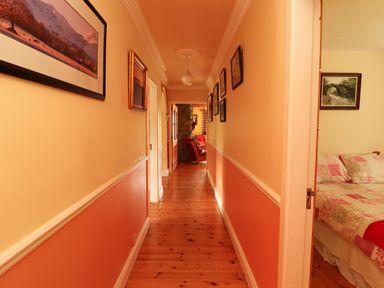 A hallway with wooden floor and framed pictures on the walls and a glimpse of a bedroom and living room at The Lodge in Churchtown near Beaufort County Kerry