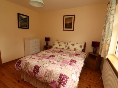 A bedroom with a double bed a chest of drawers two bedside tables with lamps and two framed pictures on the walls at The Lodge in Churchtown near Beaufort County Kerry