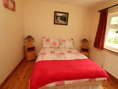 A bedroom with a bed covered with patchwork bedding and red blanket two bedside tables with lamps and a window with red curtains at The Lodge Churchtown near Beaufort County Kerry