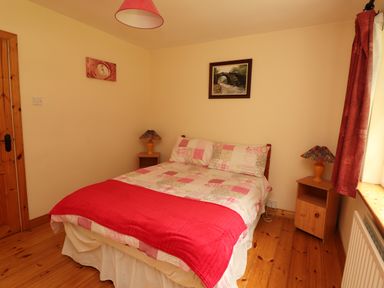 A bedroom with a double bed with patterned bedding and red throw a wooden floor and bedside tables with lamps at The Lodge in Churchtown near Beaufort County Kerry
