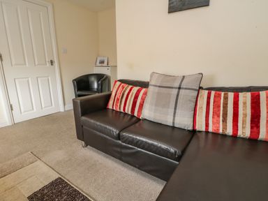 A living room with a black leather sofa with pillows and a black armchair near a closed white door at Cairns Cottage in Whitby