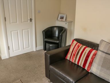 A seating area with a black leather armchair a brown leather sofa with cushions a white door and a small white cabinet at Cairns Cottage in Whitby