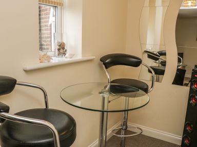 A corner with two black chairs and a round glass table near a window and a wavy mirror at Cairns Cottage in Whitby