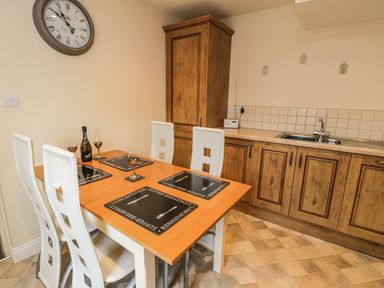 A kitchen with a dining table set with placemats and glasses next to a wooden cupboard and a sink with cabinets at Cairns Cottage in Whitby