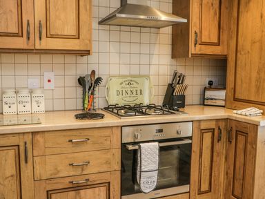 A kitchen with wooden cabinets a gas stove an oven and kitchen utensils at Cairns Cottage in Whitby