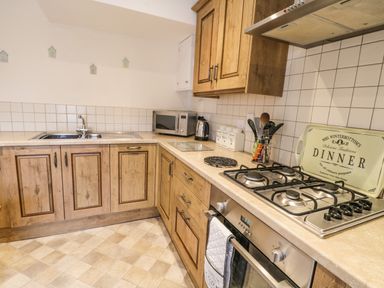A kitchen with wooden cabinets a gas stove oven a microwave kettle and a sink at Cairns Cottage in Whitby