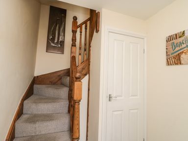 A staircase with carpet and wooden banister next to a white door with wall decorations at Cairns Cottage in Whitby