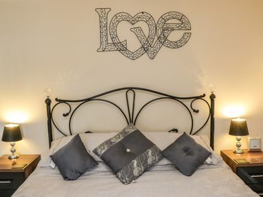 A bedroom with a black metal bed frame three pillows on the bed two bedside tables with lamps and a wall decoration spelling love at Cairns Cottage in Whitby